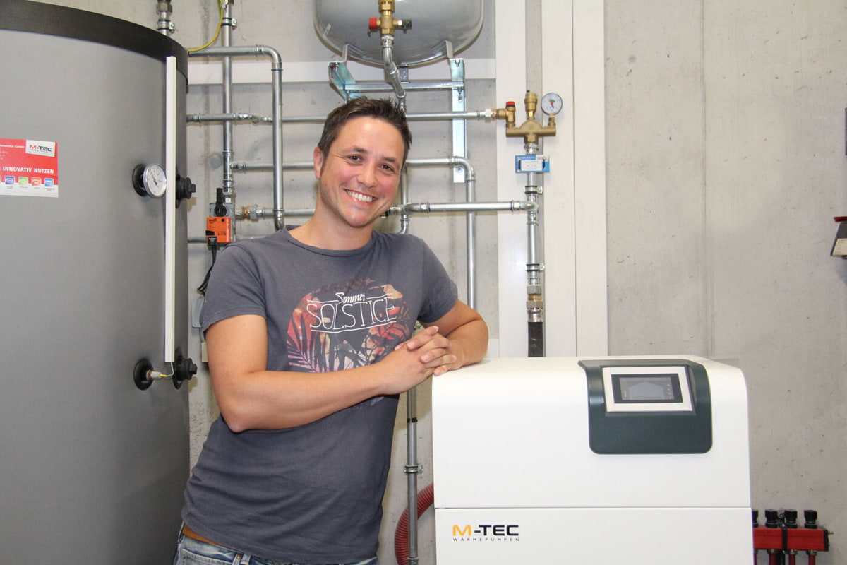 Kunde lehnt zufrieden an der M-TEC Wärmepumpe im Technikraum.